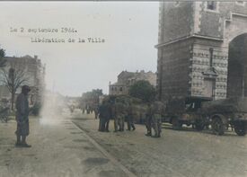 Convoi de Jeep avec remorques sur le côté gauche de la porte Notre Dame en direction de l'avenue de Valenciennes et sur la route près du convoi un attroupement de militaire américain