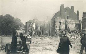 Maisons détruites près de la place au Bois, sur le devant de la photo en bas à gauche se trouve un véhicule de transport de lance à incendie et en bas à droite un couple se dirigeant sur la droite